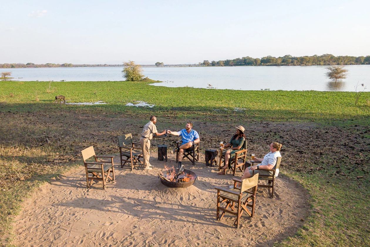 Sundowner beim Feuer in Kuthengo Camp mit Warzenschwein jenseits der Lagune