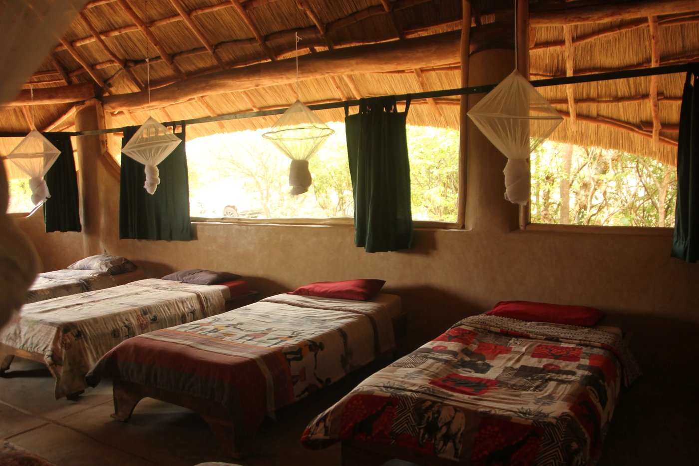 Drei Einzelbetten unter Moskitonetzen stehen in einem mit Stroh gedeckten Schlafsaal des Liwonde Safari Camp.