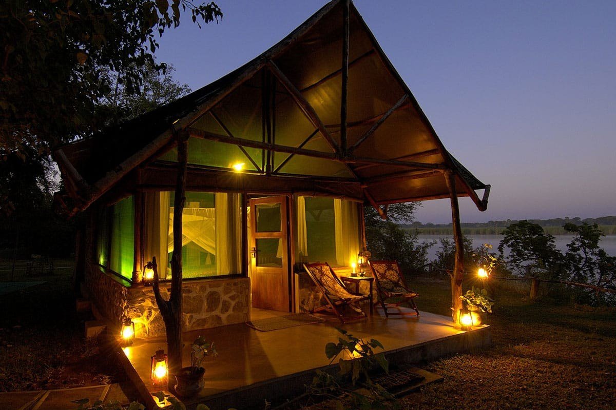 Lantern-lit stone and thatch chalet at dusk beside the river at Mvuu Camp in Liwonde
